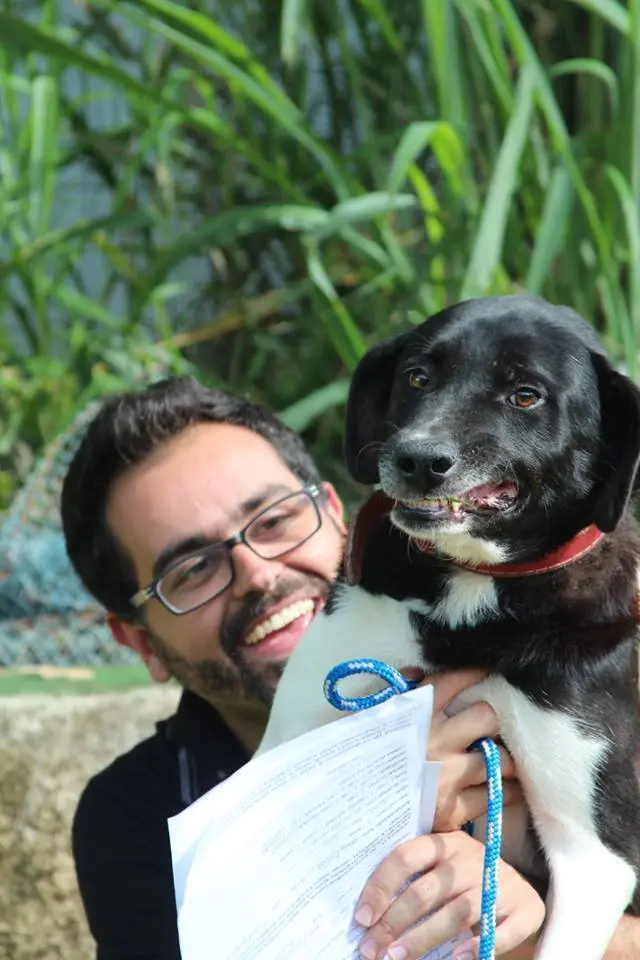 Doug finalmente com o com o protetor Francisco depois de uma longa e dolorosa espera. Descrição: O protetor Francisco tem nos braços o cão Doug, de porte médio, preto e branco. O cão parece sorrir acompanhando o largo sorriso de seu salvador. Foto: Andressa Antunes