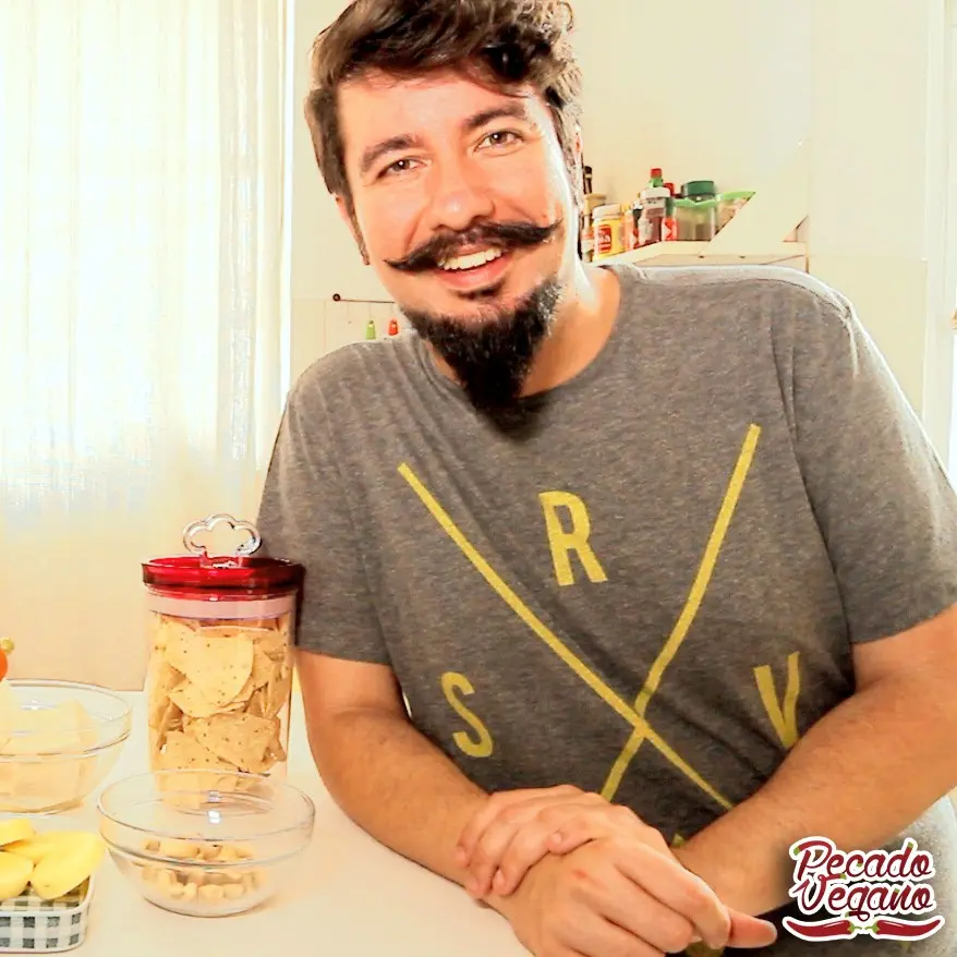 Ivan Di Simoni ficou tão empolgado com a culinária vegana que até criou um programa. Descrição para deficientes físicos: O Chef vegano Ivan aparece encostado em uma mesa sorrindo. Ele tem pele clara, cabelos escuros e levemente ondulados, barba e bigode. Foto: Divulgação