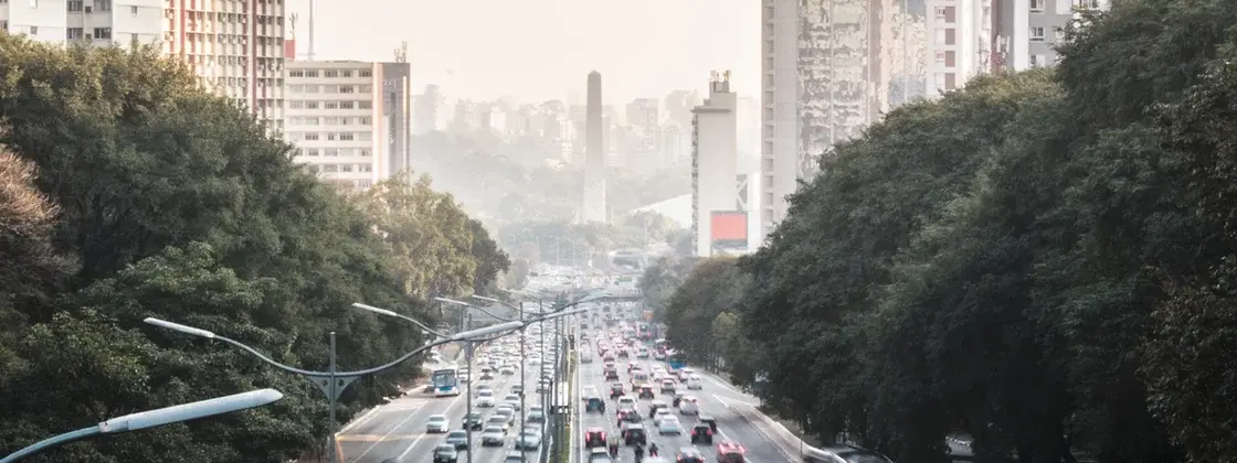 A imagem mostra rodovias de uma cidade com diversos carros e área verde aos arredores.