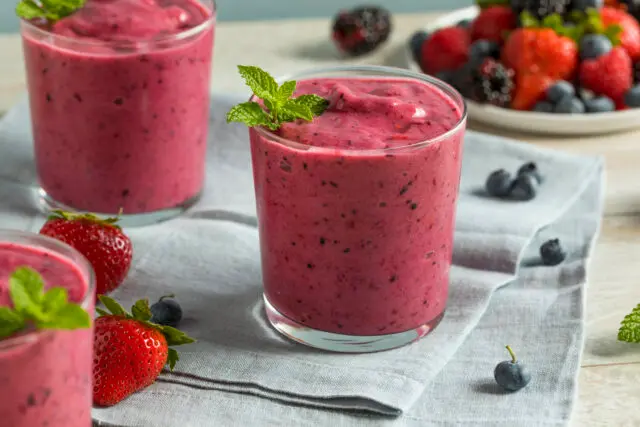 Bebida de frutas, avermelha, dentro de um copo de vidro e decorada com uma folha de hortelã.